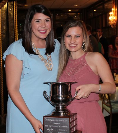 Two individuals standing indoors holding a trophy